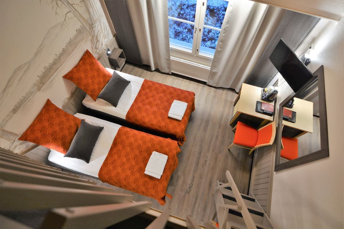 Una habitación con dos camas, un escritorio, una silla y una ventana con cortinas.