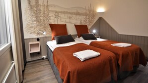 A hotel room with two beds, a mural of a forest, a small bedside table, and a wall-mounted light. - Hotel Ylläsrinne (Kolari)