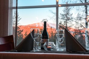A table set with wine glasses, a bottle, and a candle, with a view of a mountain through a window. - Hotel Ylläsrinne (Kolari)