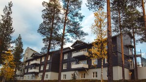 A multi-story hotel with balconies, surrounded by tall trees and a hilly landscape. - Hotel Ylläsrinne (Kolari)
