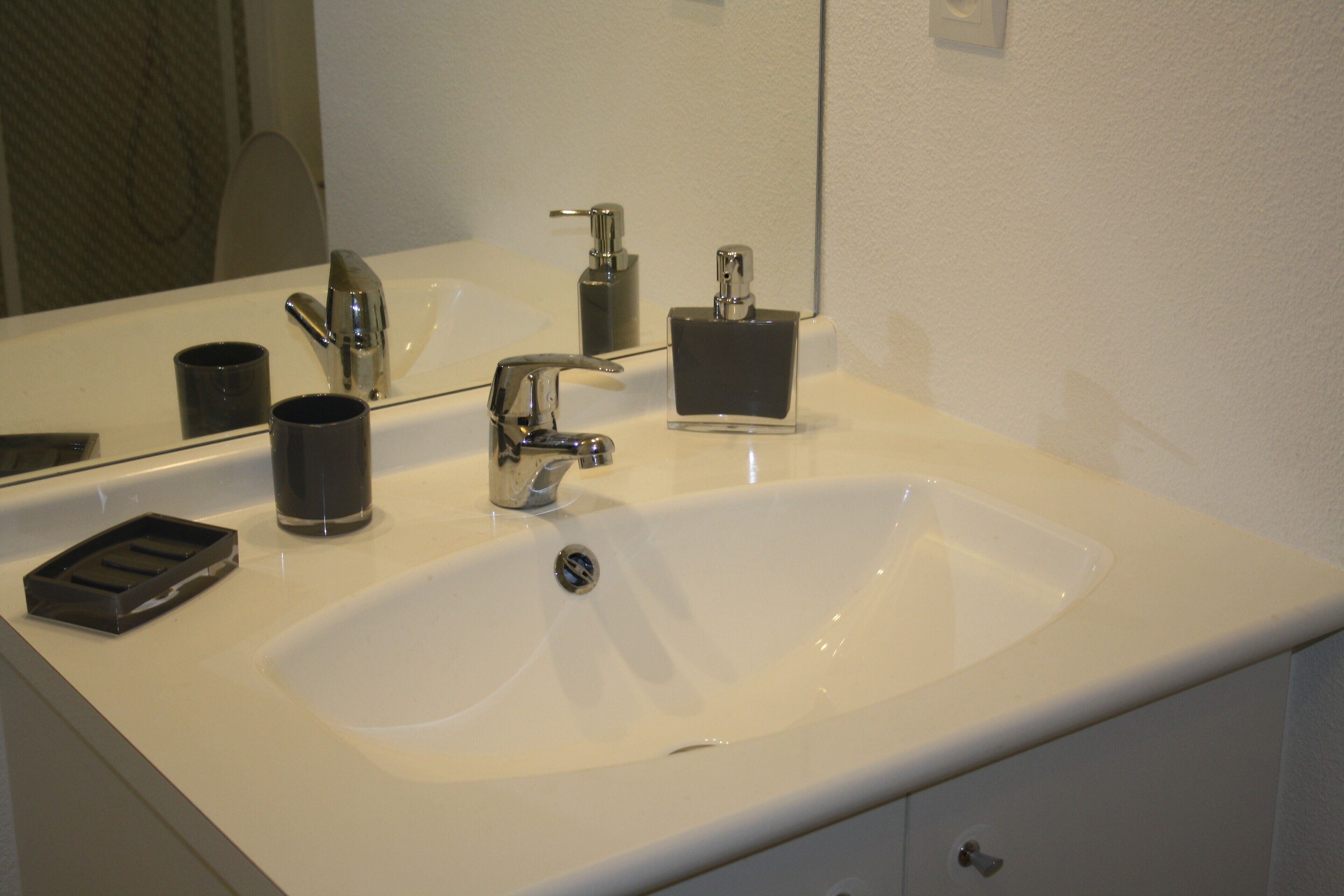 A bathroom with a white sink, a mirror, a faucet, and a soap dispenser.