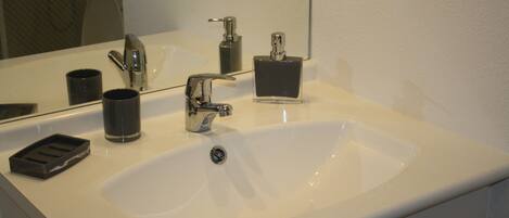 A bathroom with a white sink, a mirror, a faucet, and a soap dispenser.