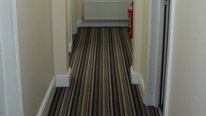A narrow hallway with a striped carpet, a radiator, and a painting on the wall. - New Globe Hotel (London)