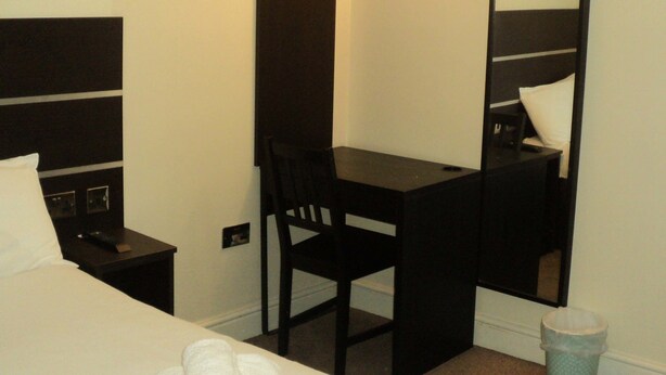 A hotel room with a bed, a desk, a chair, a mirror, and a trash bin. - New Globe Hotel (London)