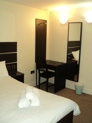 A hotel room with a bed, a desk, a chair, a mirror, and a trash bin. - New Globe Hotel (London)