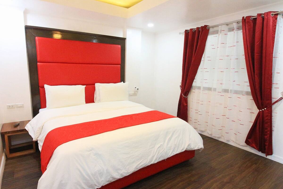 A hotel room with a large bed, red curtains, and a white headboard.