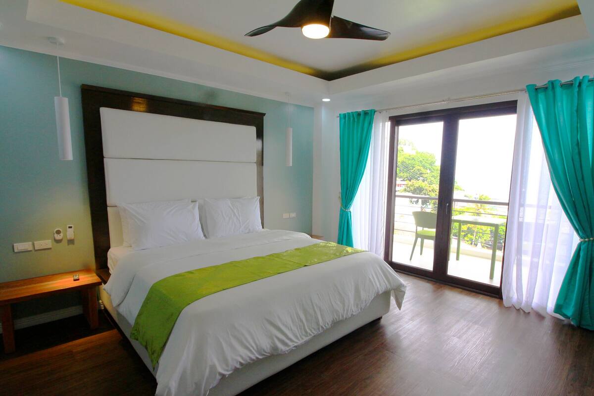 A hotel room with a large bed, a ceiling fan, and a view of the outdoors through a sliding glass door.