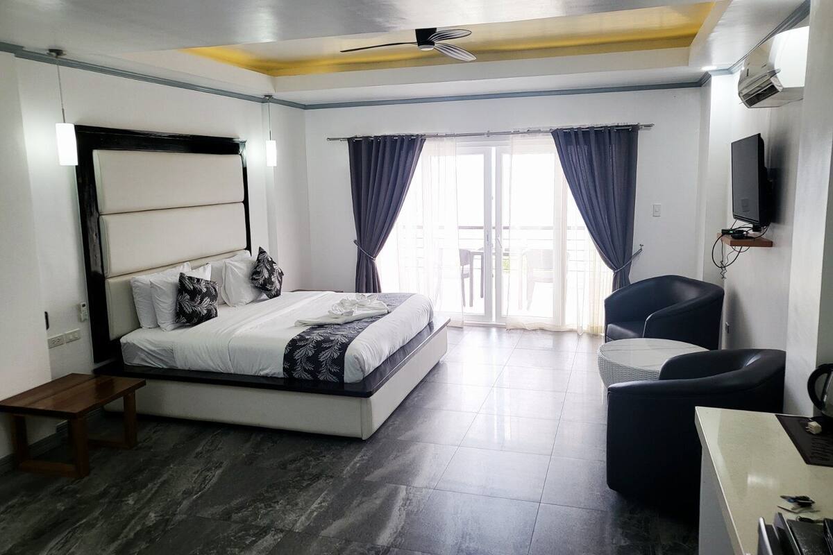 A modern hotel room with a large bed, a desk, a chair, a ceiling fan, and a TV.