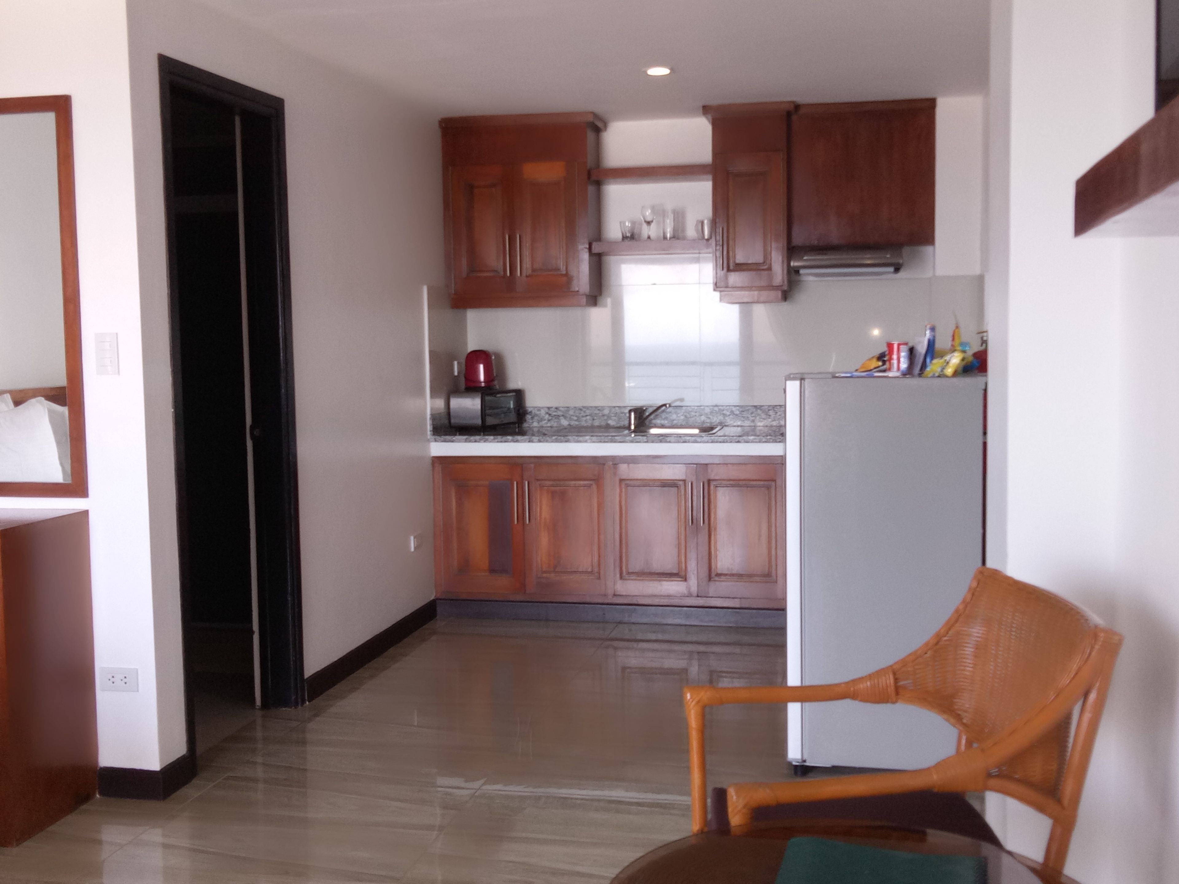 Una cocina moderna con armarios de madera, un refrigerador de acero inoxidable y una zona de comedor con una silla de mimbre.