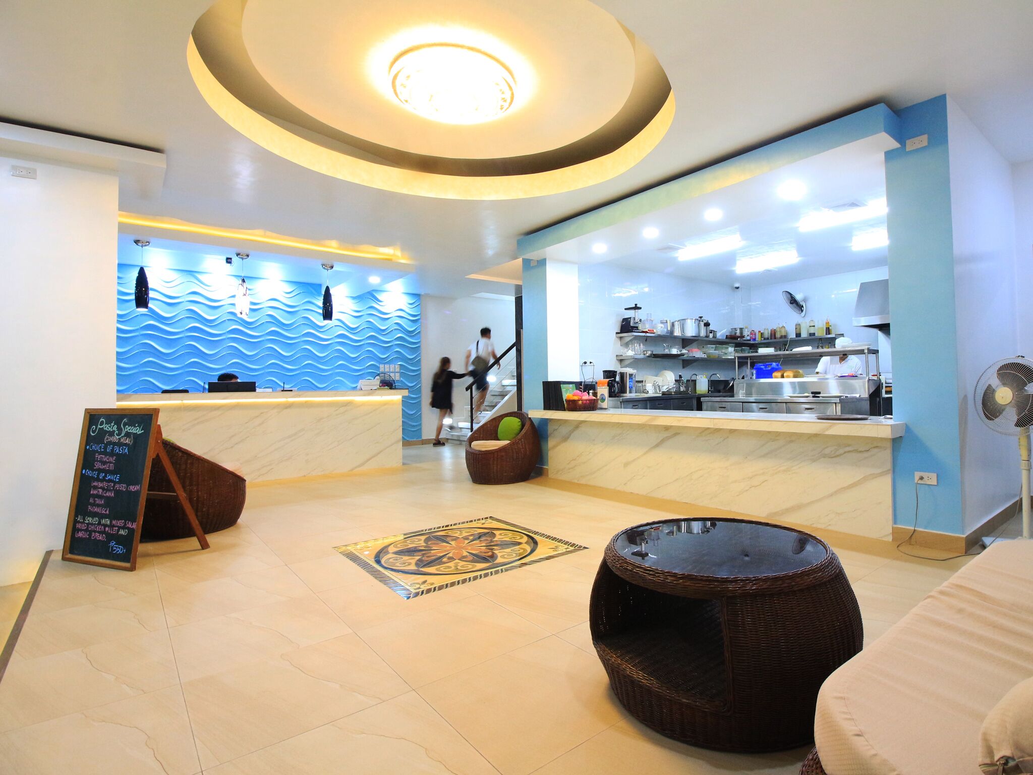 A modern restaurant interior with a central counter, seating area, and a kitchen visible in the background.