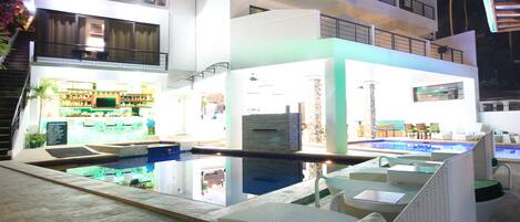 Un hotel moderno con zona de piscina, asientos exteriores y un bar.