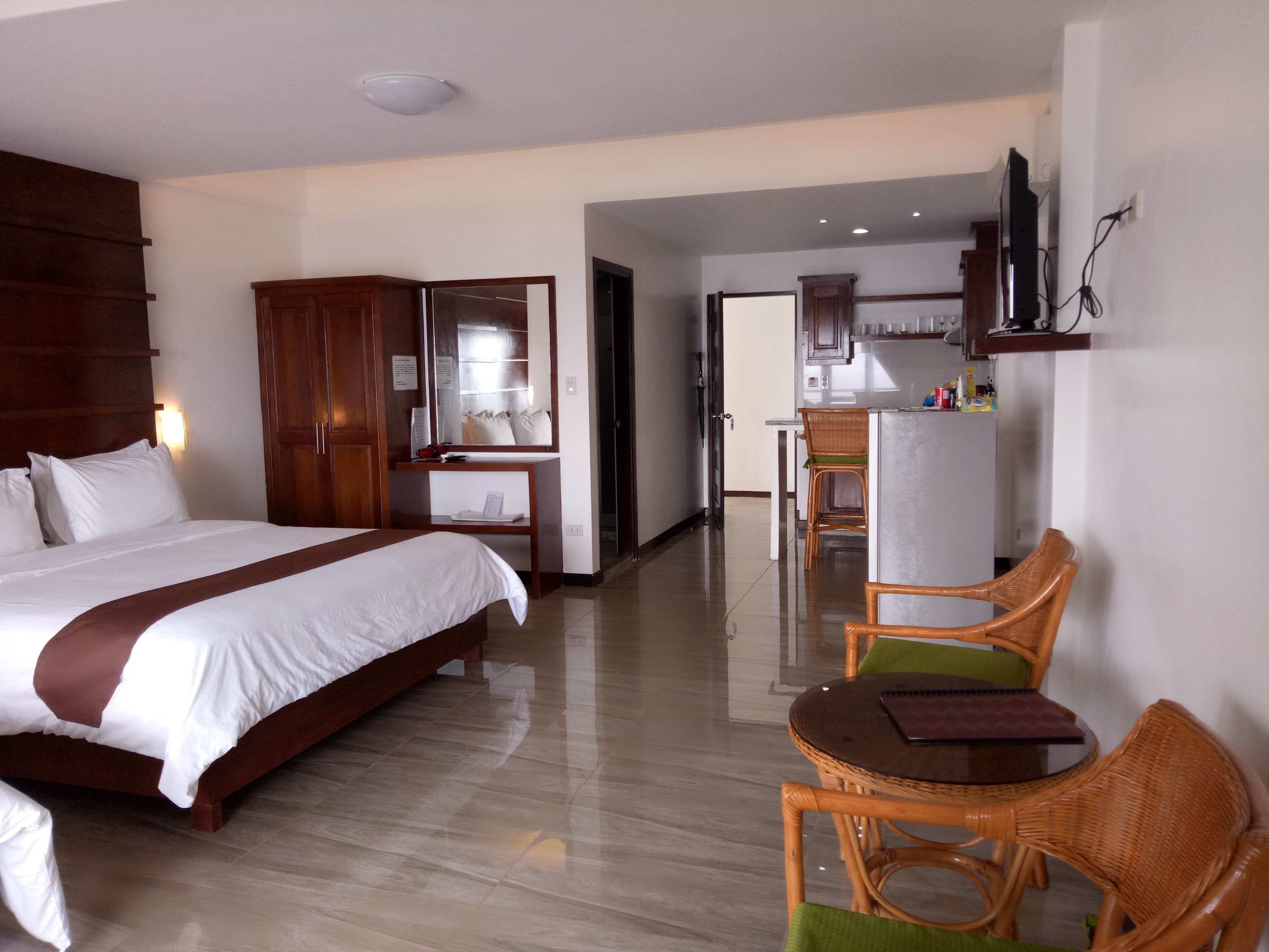 Una habitación de hotel con cama, escritorio, silla, espejo y kitchenette.