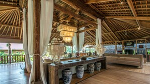 Amplia habitación con techo de madera, una larga encimera con jarrones decorativos y vistas al exterior con vegetación.