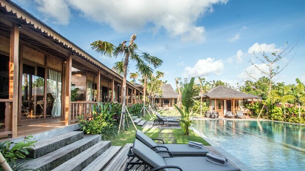 Un resort con piscina, terraza de madera, sillas de descanso y plantas tropicales.