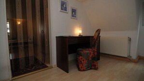 A room with a wooden floor, a desk with a chair, a radiator, and two framed pictures on the wall. - Hotel Hirsch (Fulda)