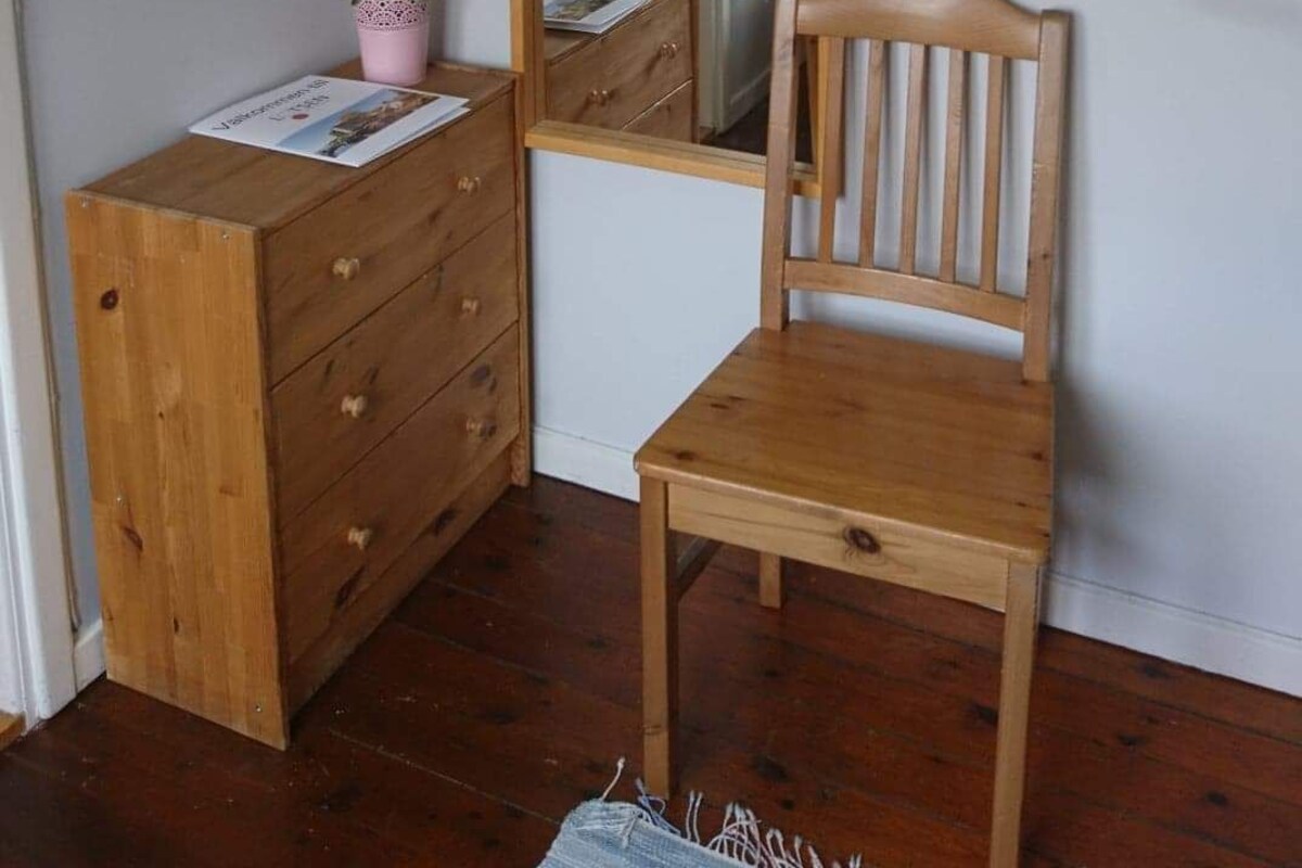 A room with a wooden dresser, a chair, a mirror, and a hanging rack.
