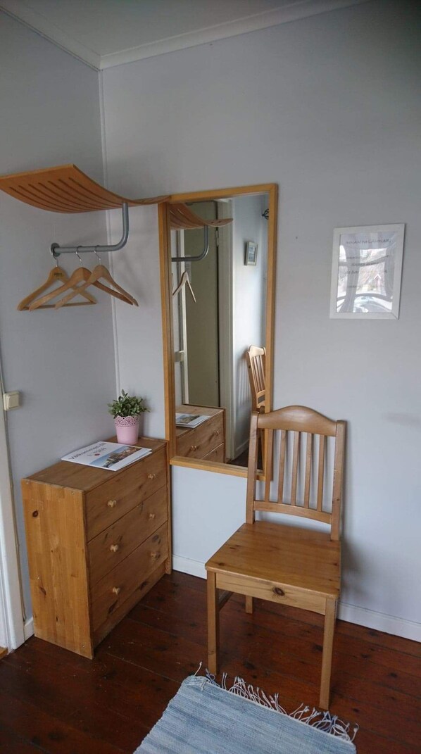 Une pièce comprenant une commode en bois, une chaise, un miroir et un porte-vêtements suspendu.