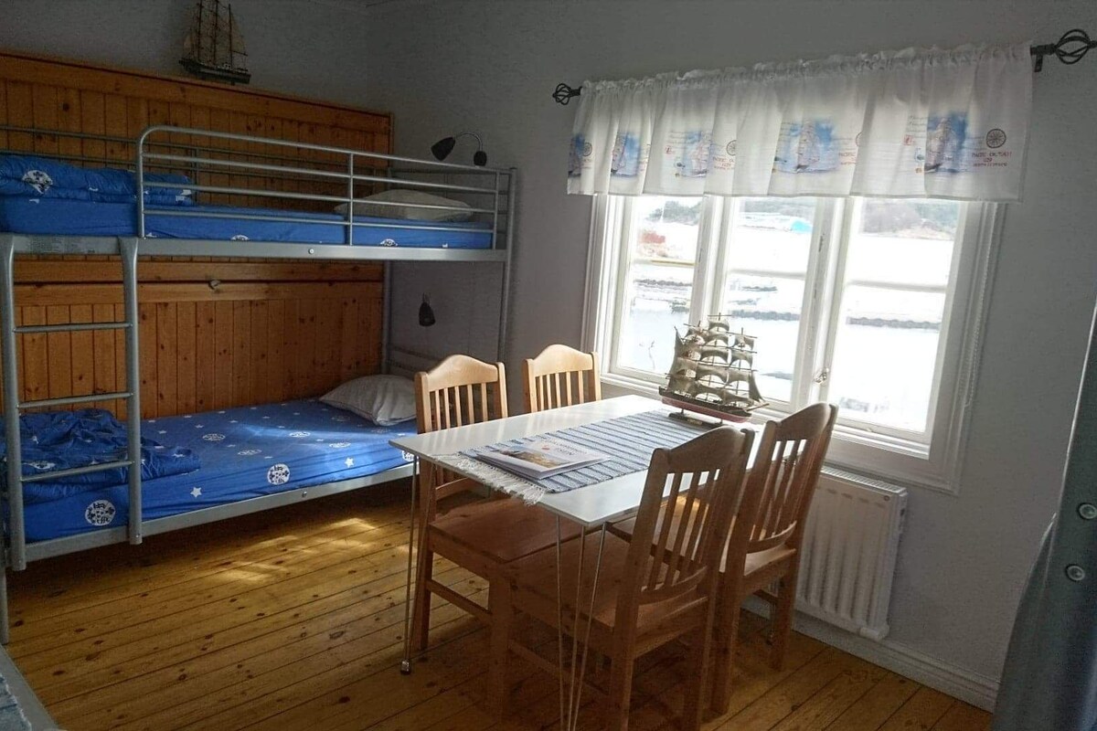 A bunk bed room with a table and chairs, wooden flooring, and a window with a view of the water.