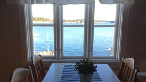 A dining table with chairs, a potted plant, and a view of a lake through large windows. - Hostel Lotsen (Dalaro)