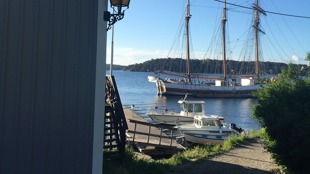 A harbor with a large sailing ship docked, a smaller boat, and a building with a lantern. - Hostel Lotsen (Dalaro)