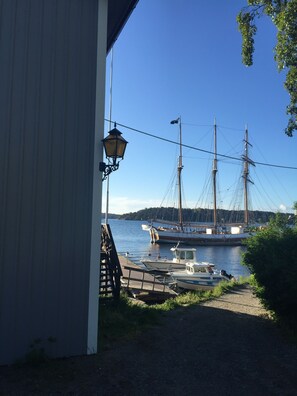 Un port où est amarré un grand voilier, ainsi qu’un plus petit bateau, et un bâtiment surmonté d’une lanterne.