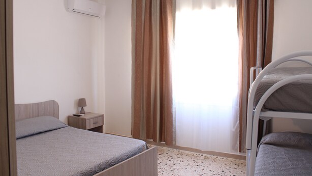 Un dormitorio con una cama individual superpuesta, una mesita de noche con lámpara y una ventana con cortinas.