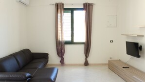 Una sala de estar moderna con un sofá de cuero negro, un mueble de televisión de madera y una ventana con cortinas.