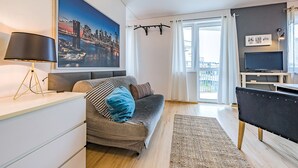 Un salon moderne avec un canapé, un téléviseur, une lampe et un grand tableau représentant un paysage urbain.