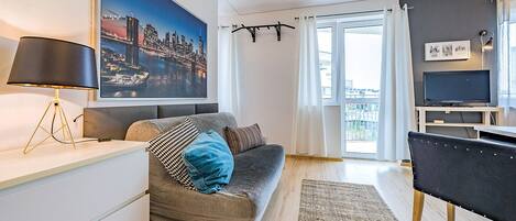 A modern living room with a sofa, a TV, a lamp, and a large cityscape painting.