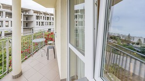 Un balcon avec une table et des chaises, une vue sur un immeuble en construction et une balustrade ornée de fleurs.