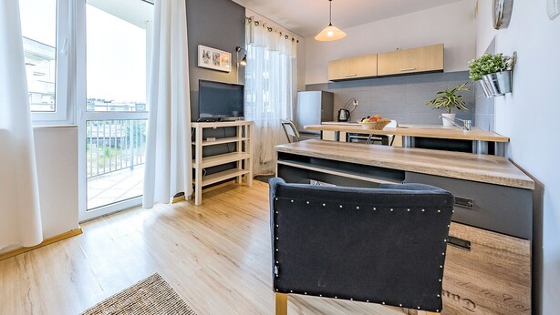 Une cuisine moderne avec un coin repas, un téléviseur posé sur un meuble et une vue sur le balcon extérieur.