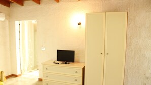 Una habitación con un armario blanco, un televisor sobre una cómoda y una puerta con cortina.