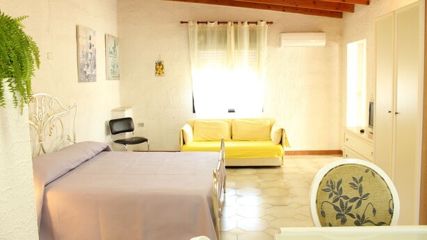 Un dormitorio con una cama, un sofá amarillo, una silla y un baño con inodoro.