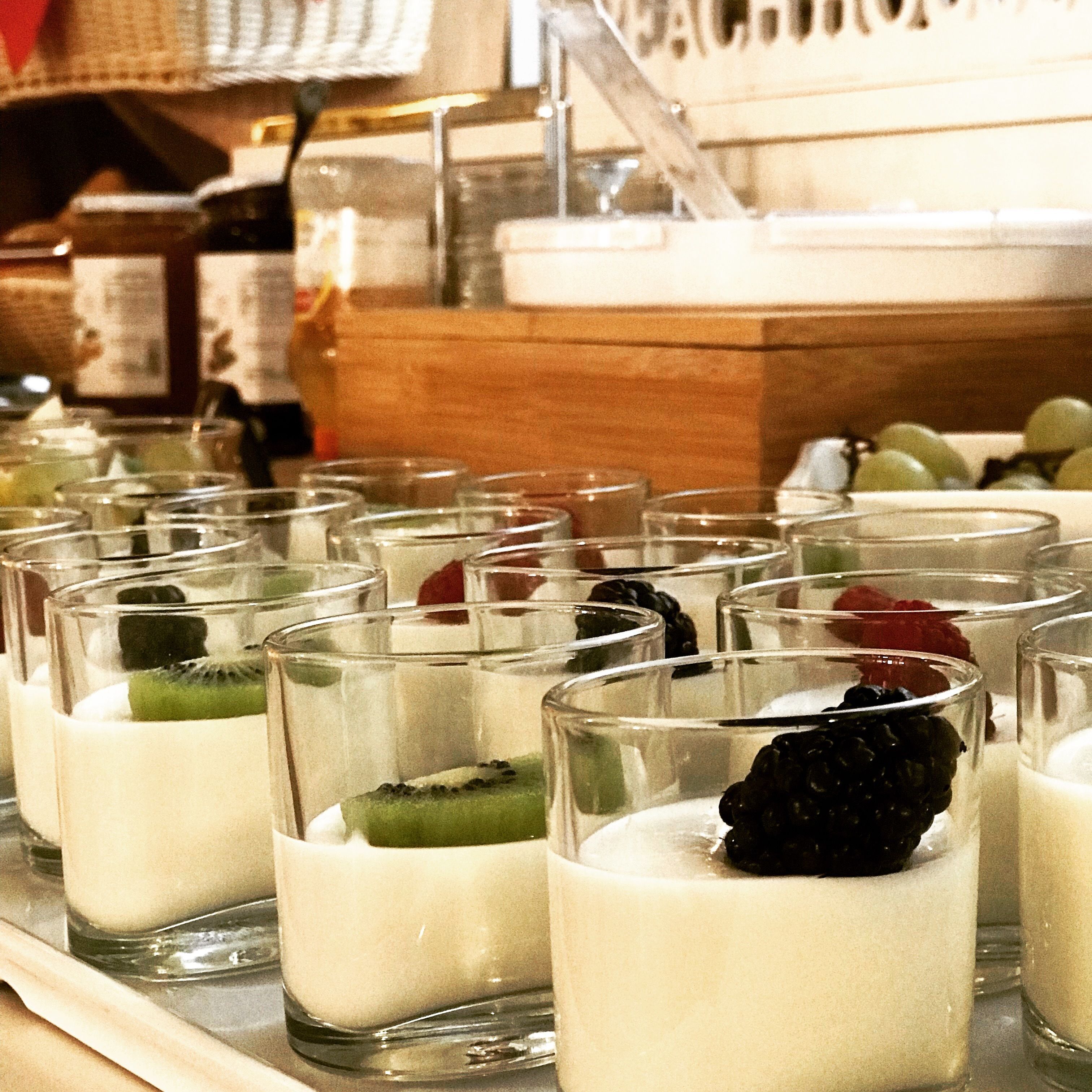 Una fila di bicchierini dessert con frutta su un vassoio.