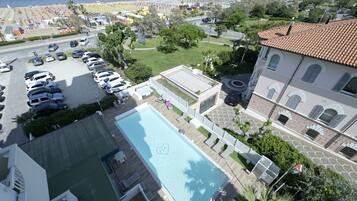 A hotel with a swimming pool, a parking lot, and a view of the beach.