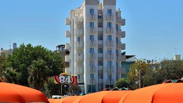 Un hôtel à plusieurs étages doté de balcons, entouré de parasols orange et de palmiers.