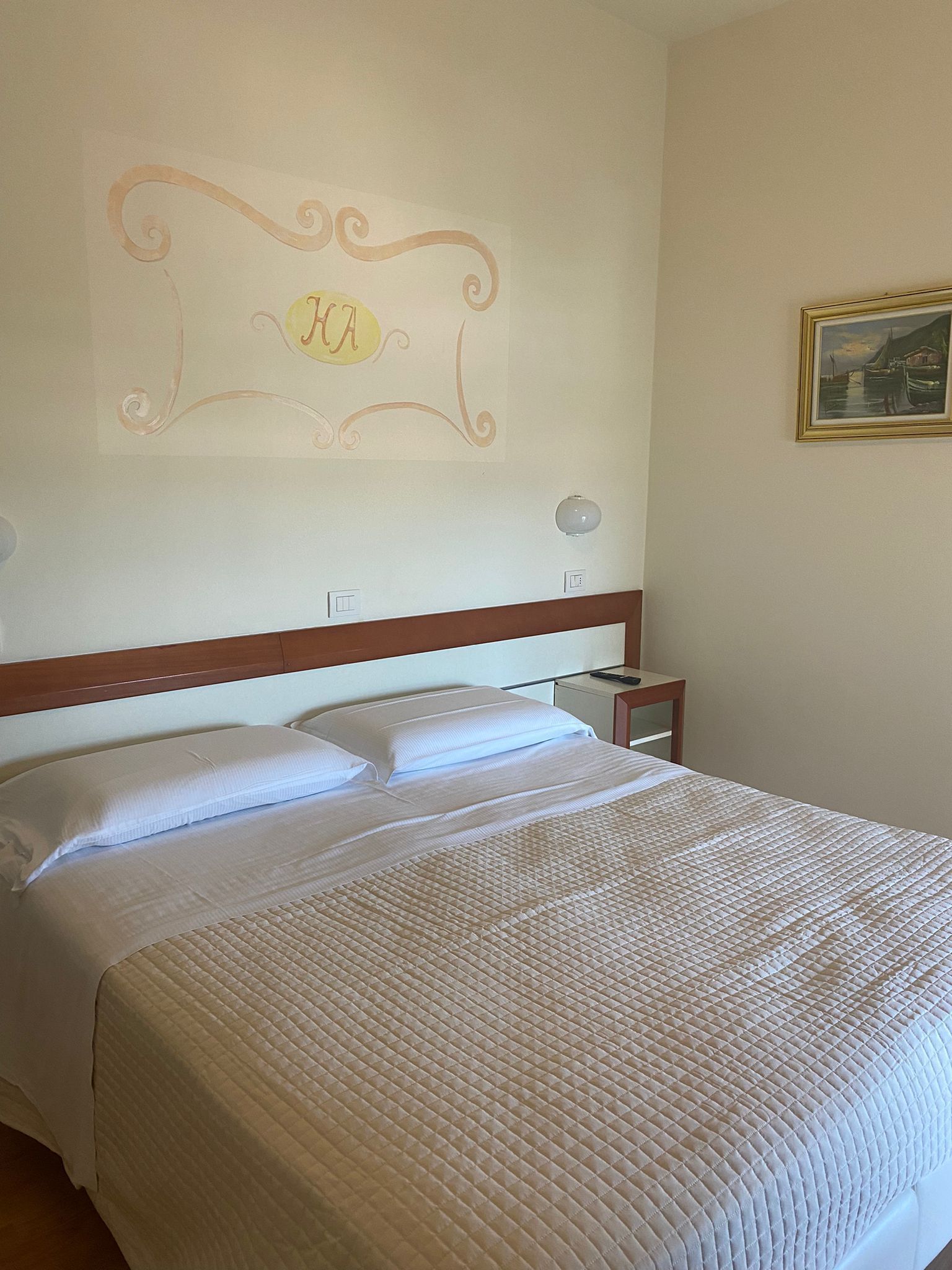 Een net opgemaakt bed met een gewatteerde spreideken, een houten hoofdbord en een decoratie aan de muur erboven.