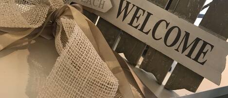 A wooden sign with "WELCOME" and "TO THE BEACH" written on it, tied with a burlap ribbon.
