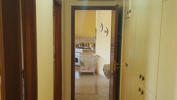 Un pasillo que conduce a una cocina con suelo de baldosas, puertas de madera y un equipo de aire acondicionado en la pared.