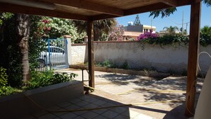 Uma área externa coberta com piso de azulejos, um portão azul e uma mangueira no chão.