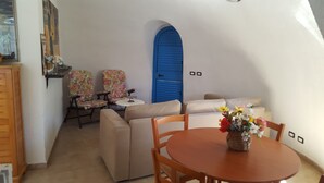 Um quarto acolhedor com uma mesa redonda de madeira, duas poltronas florais, um sofá e uma porta azul.