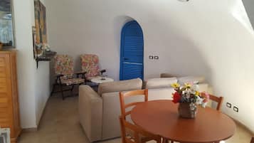 Um quarto acolhedor com uma mesa redonda de madeira, duas poltronas florais, um sofá e uma porta azul.