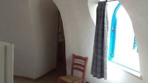 Quarto com teto alto em arco, uma cadeira de madeira, janela com cortinas e luminária visível.