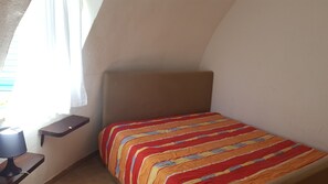 A small, single-bed room with a plain headboard, a bedside table, and a window with curtains. - Bungalow Tonnarella Beach (Mazara del Vallo)