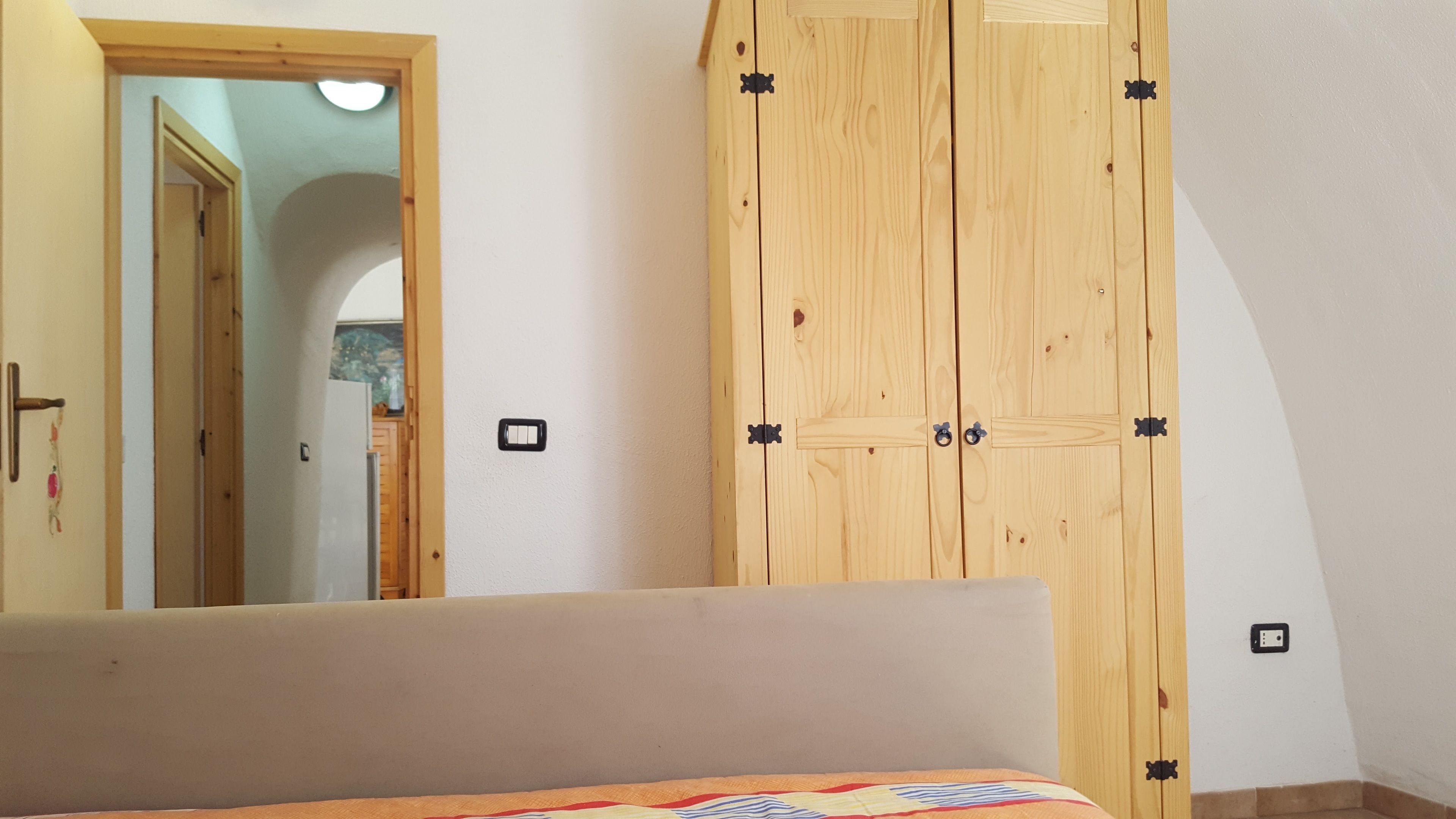 Quarto com cama, guarda-roupa de madeira e porta para outro cômodo.