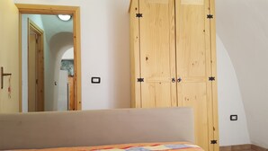 Quarto com cama, guarda-roupa de madeira e porta para outro cômodo.