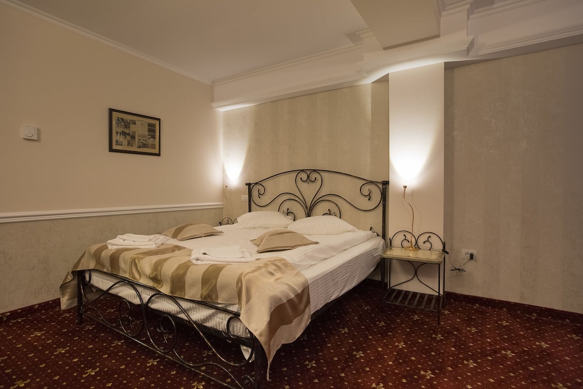 Un lit bien fait, recouvert d’une couverture à rayures, une table de chevet avec une lampe et un tableau encadré au mur.
