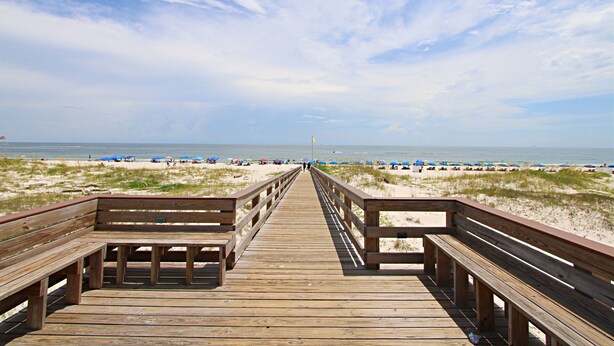 A wooden boardwalk leading to a beach with sand dunes and beach umbrellas. - Time to get… 🎶 Knee deep in the water somewhere! 🎶 on island time! (Gulf Shores)