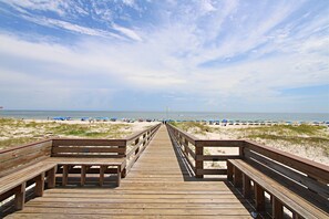 A wooden boardwalk leading to a beach with sand dunes and beach umbrellas.