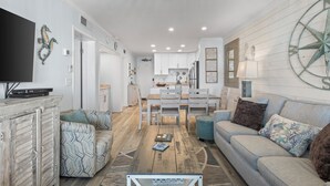 A spacious living area with a wooden coffee table, a sofa, and a TV on a cabinet. - Time to get… 🎶 Knee deep in the water somewhere! 🎶 on island time! (Gulf Shores)